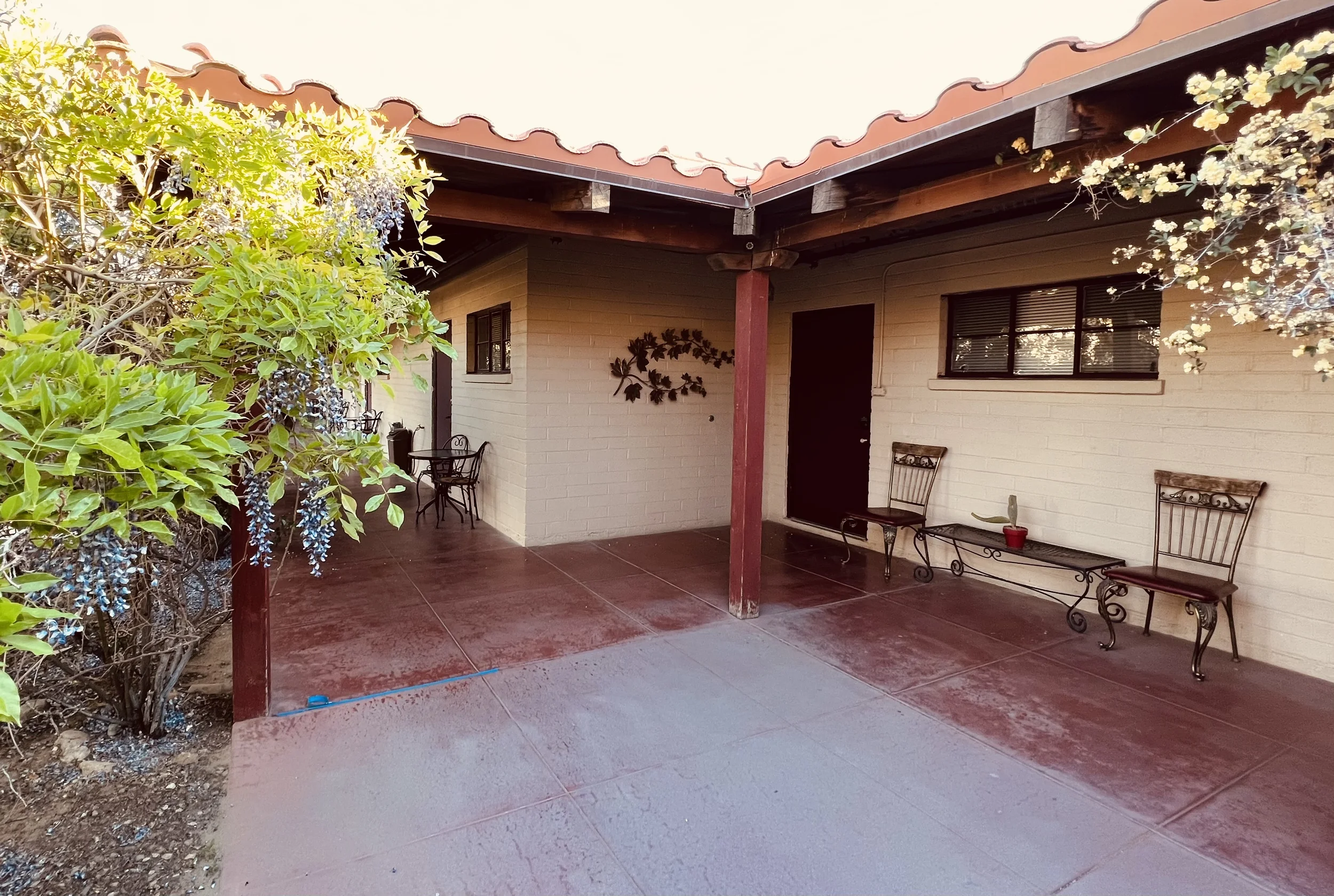 A covered patio with bushes to the left and a door to a room.  