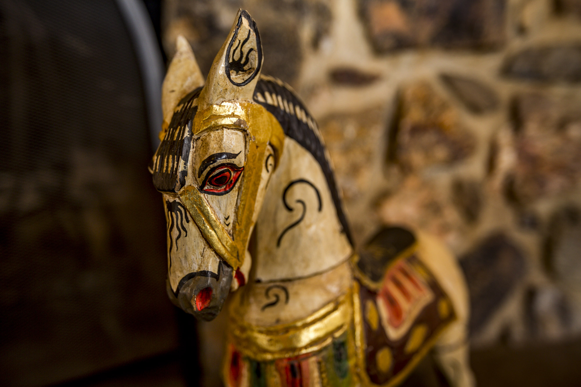 An antique wooden horse with a stone wall behind it.