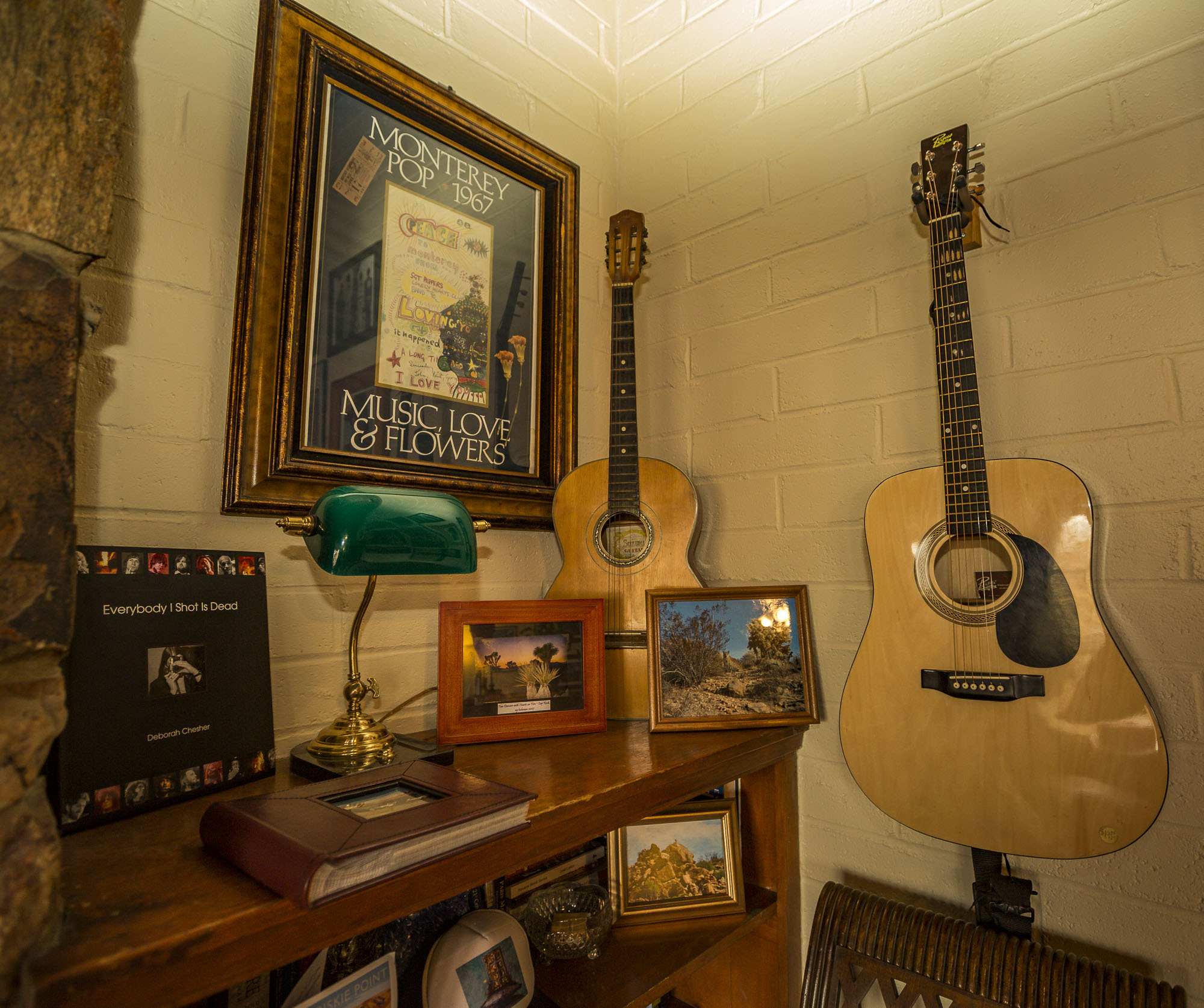 the top of a book shelf with a concert photo, guitars and a lamp. 